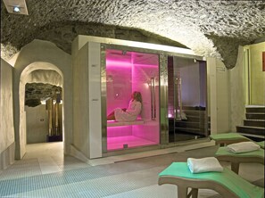 Une salle de spa avec un plafond en pierre, un fauteuil de massage éclairé en rose et un espace d’accueil doté d’un escalier.