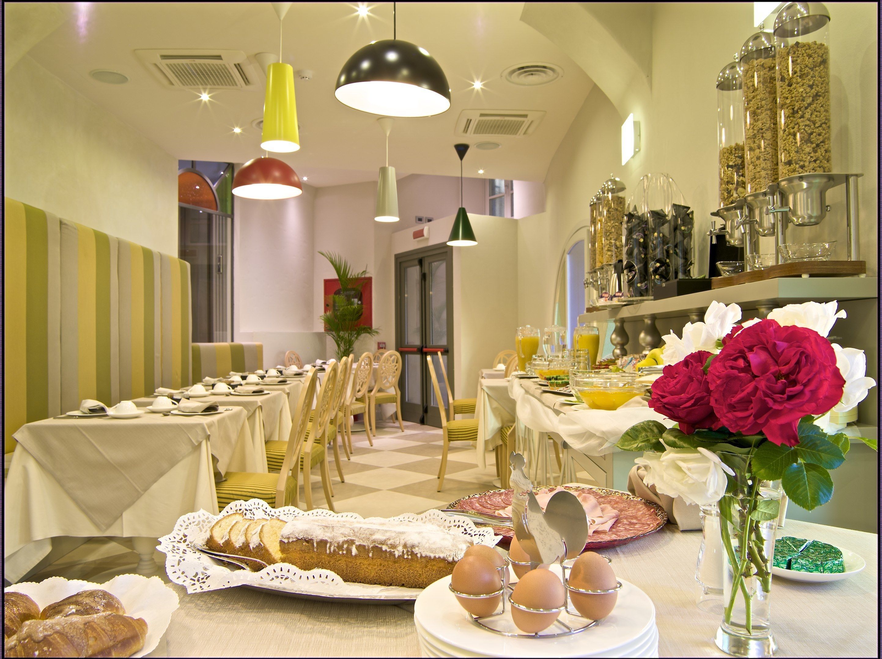 Un bufé de desayuno con diferentes alimentos, un florero con flores y un comedor con sillas y mesas.