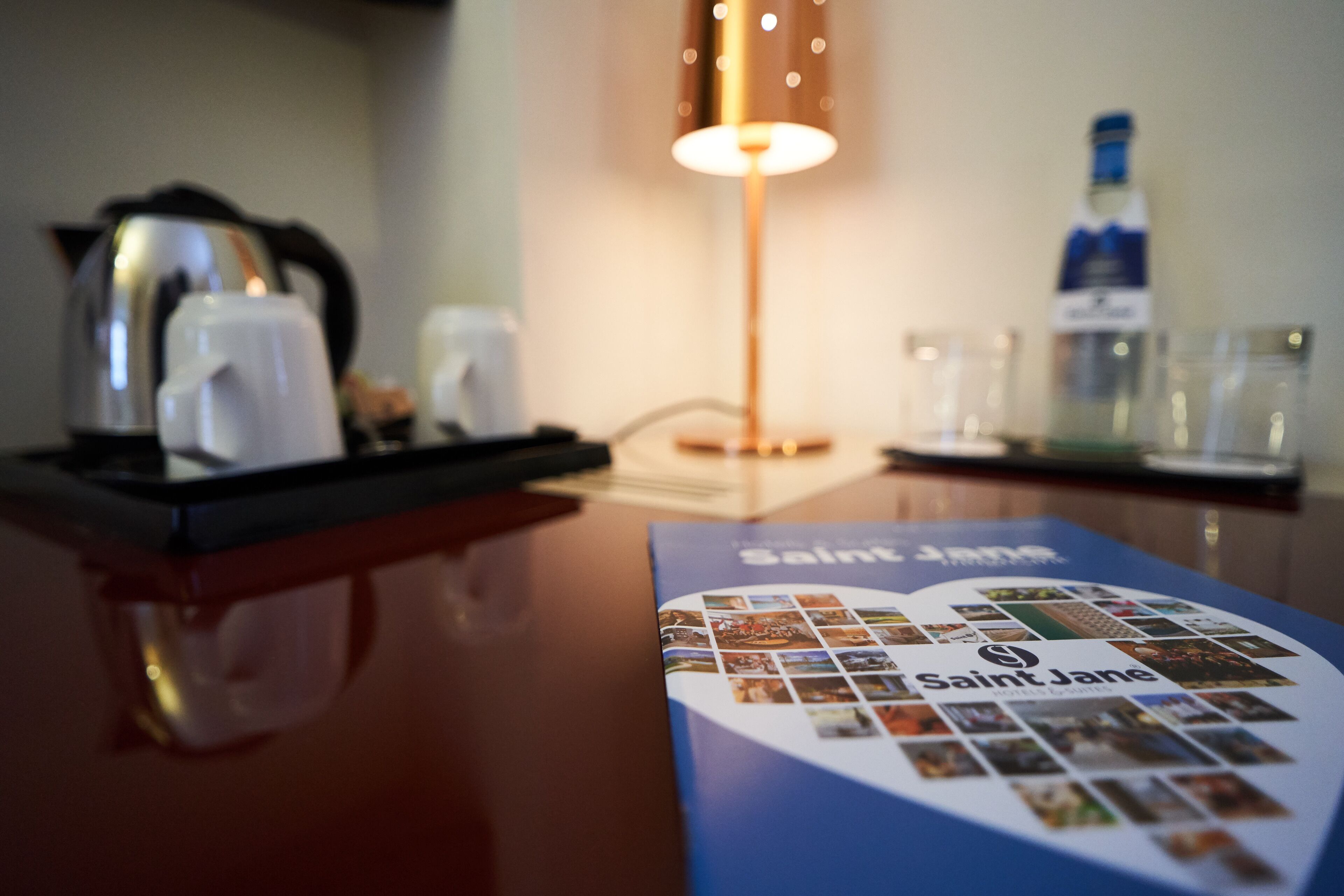 Een hotelkamer met een koffiezetapparaat, een fles water en een brochure op tafel.