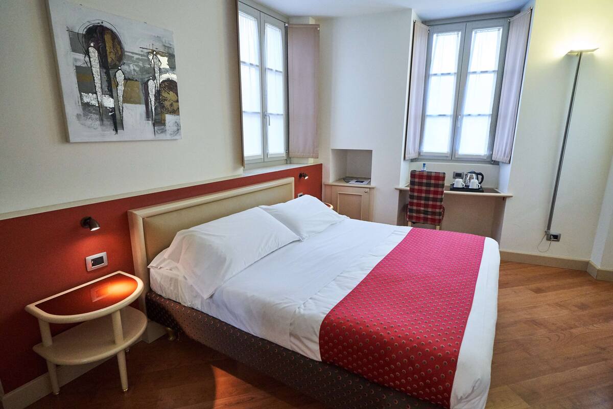 A hotel room with a bed, bedside table, and a small desk with a chair.
