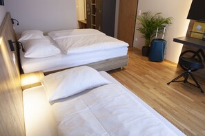 A hotel room with two single beds, a desk, a chair, a potted plant, and a suitcase. - JUFA Hotel Erlaufsee (Mariazell)