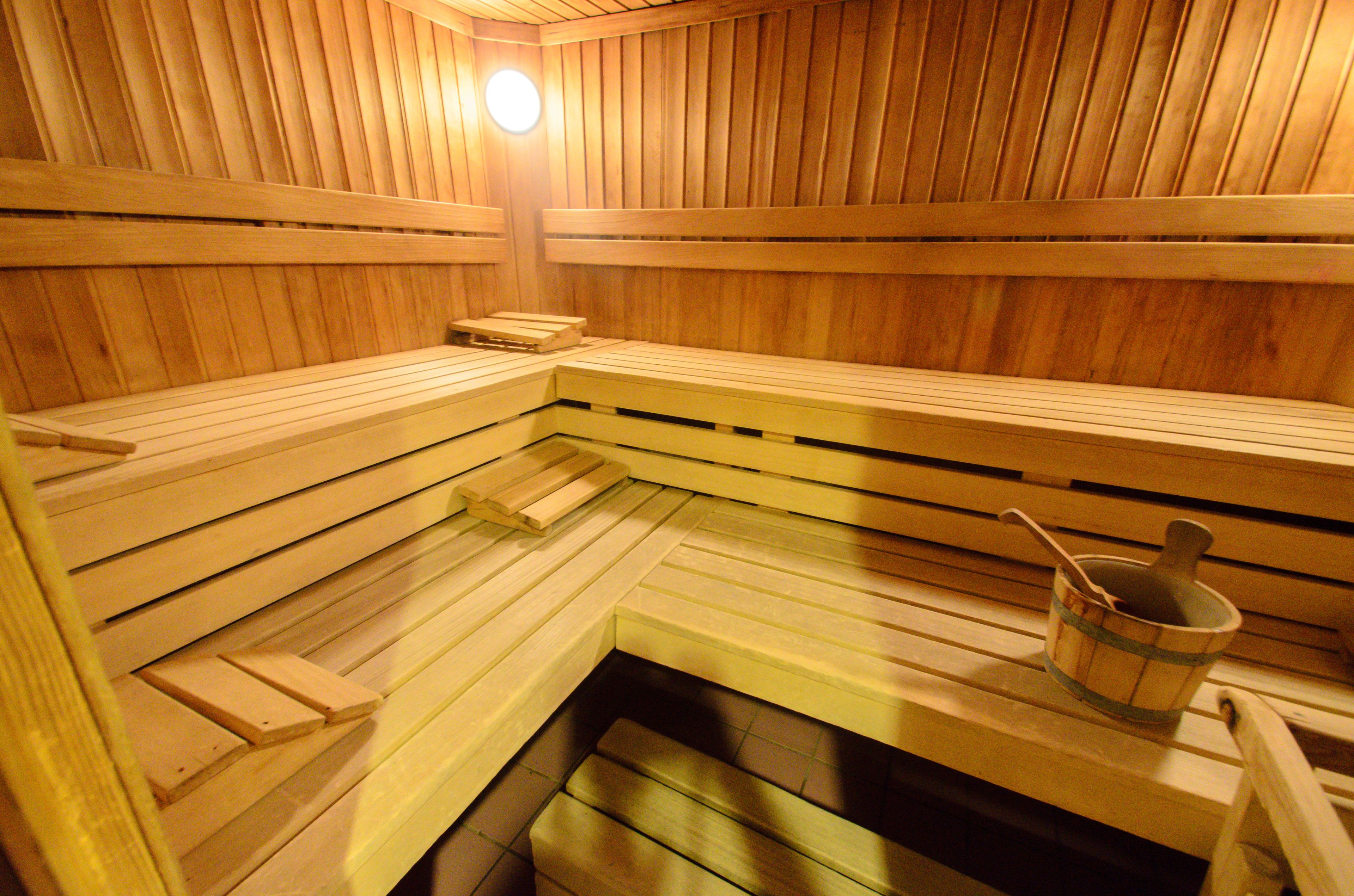 Una sauna con bancos de madera y un cubo de madera con una cuchara.