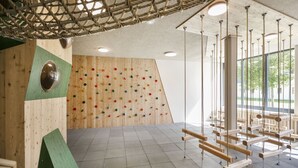 A climbing wall with colorful holds, a wooden climbing area, and a large window with a view of trees. - JUFA Hotel Erlaufsee (Mariazell)