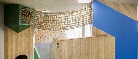 Un interior de madera con una pared de escalada, una red de cuerda y una pared azul.