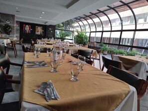 A restaurant with tables set for dining, a large window with a view, and a mural on the wall.