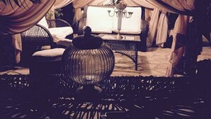 A cozy, dimly lit room with a bed covered in white drapes, a small table with a vase, and a chair.