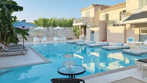 A swimming pool with lounge chairs and umbrellas, surrounded by a fence and vegetation.