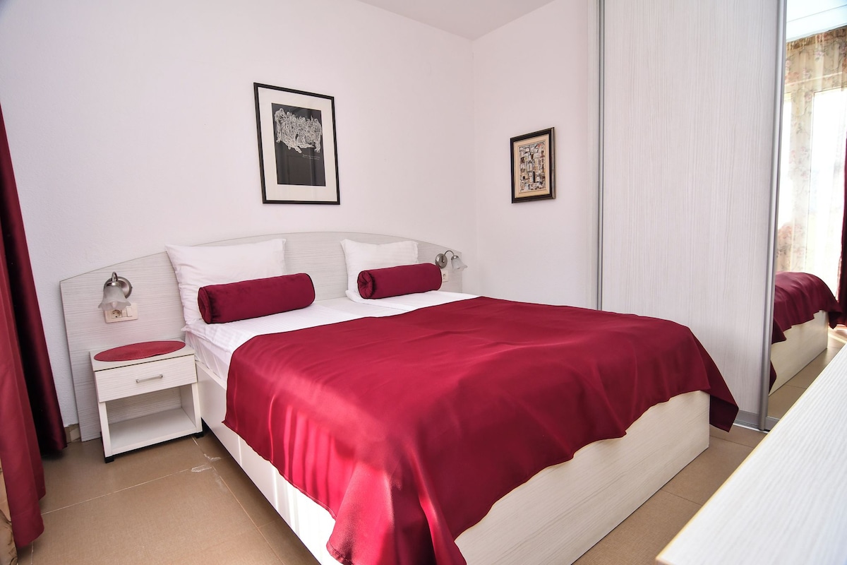 A neatly arranged hotel room with a large bed, a bedside table, a mirror, and two framed pictures on the wall.