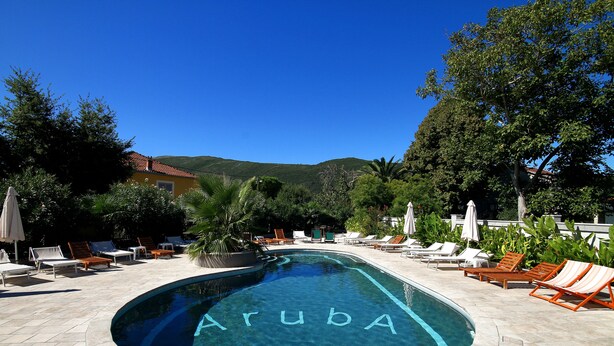 Una piscina con la palabra "Aruba" escrita en el agua, rodeada de sillas de descanso y sombrillas.