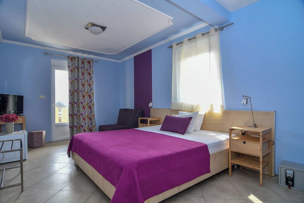 A bedroom with a bed, a desk, a chair, a TV, and a window with curtains.