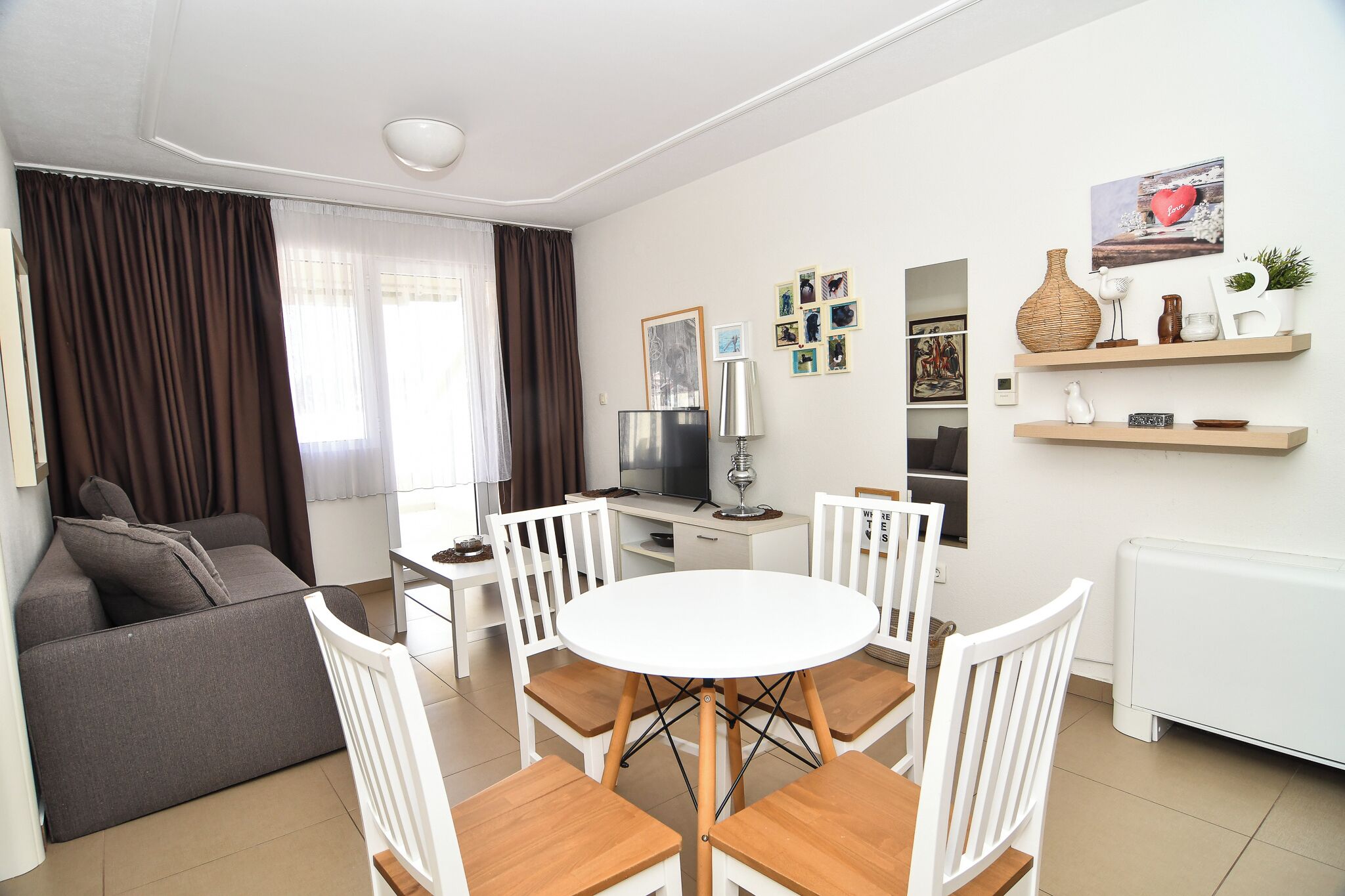 Un salon moderne comprenant un canapé, une table à manger, des chaises, un téléviseur et des objets décoratifs.