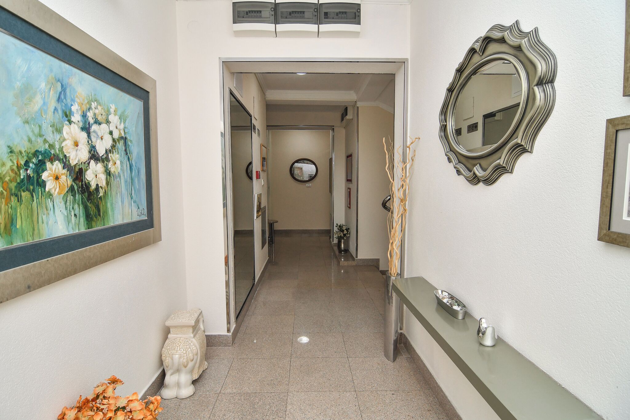 A hallway with a painting, a mirror, and a vase.