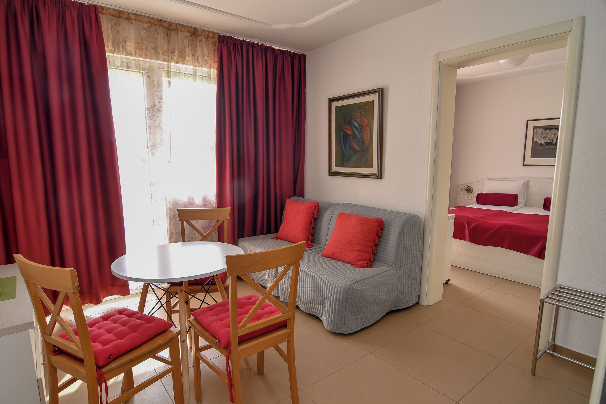 A room with a dining table, chairs, a sofa, a bed, and a painting on the wall.