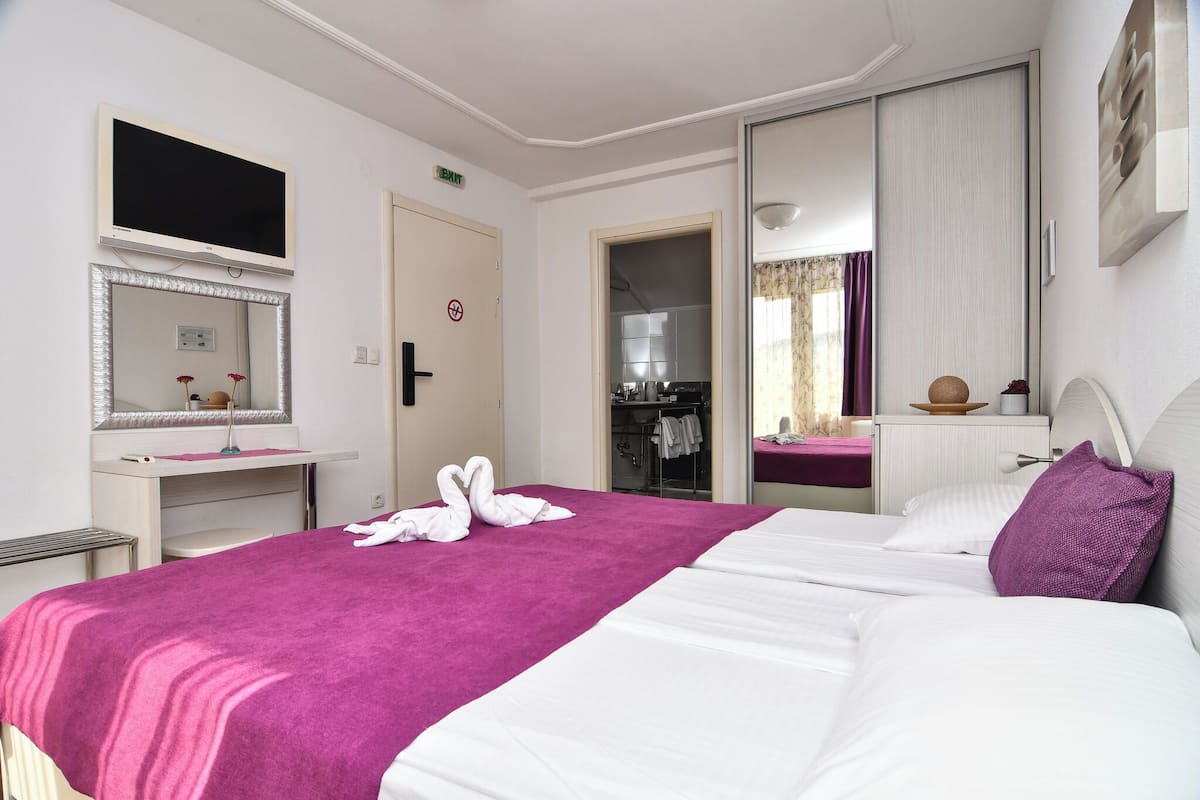A hotel room with a bed, a desk, a mirror, a wardrobe, and a bathroom visible through an open door.