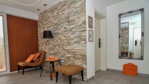 Una sala de estar moderna con una pared de piedra, un sofá, una mesita, una lámpara de pie, un espejo y un atril para revistas.