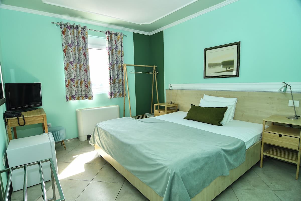 A bedroom with a bed, a television, a radiator, a window with curtains, and a picture on the wall.