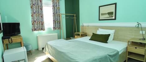 A bedroom with a bed, a television, a radiator, a window with curtains, and a picture on the wall.
