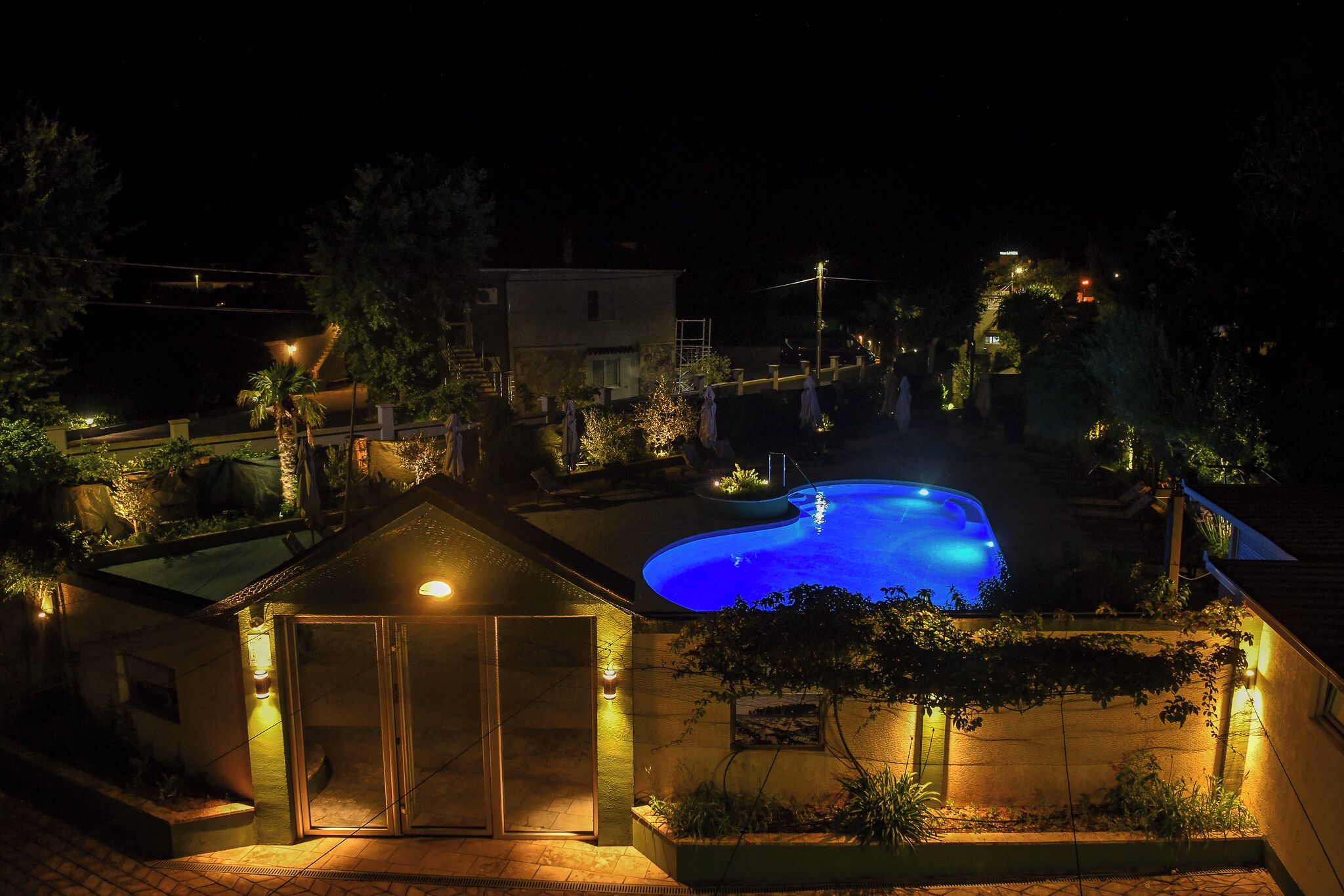 Piscina à noite com edifícios e árvores ao redor.