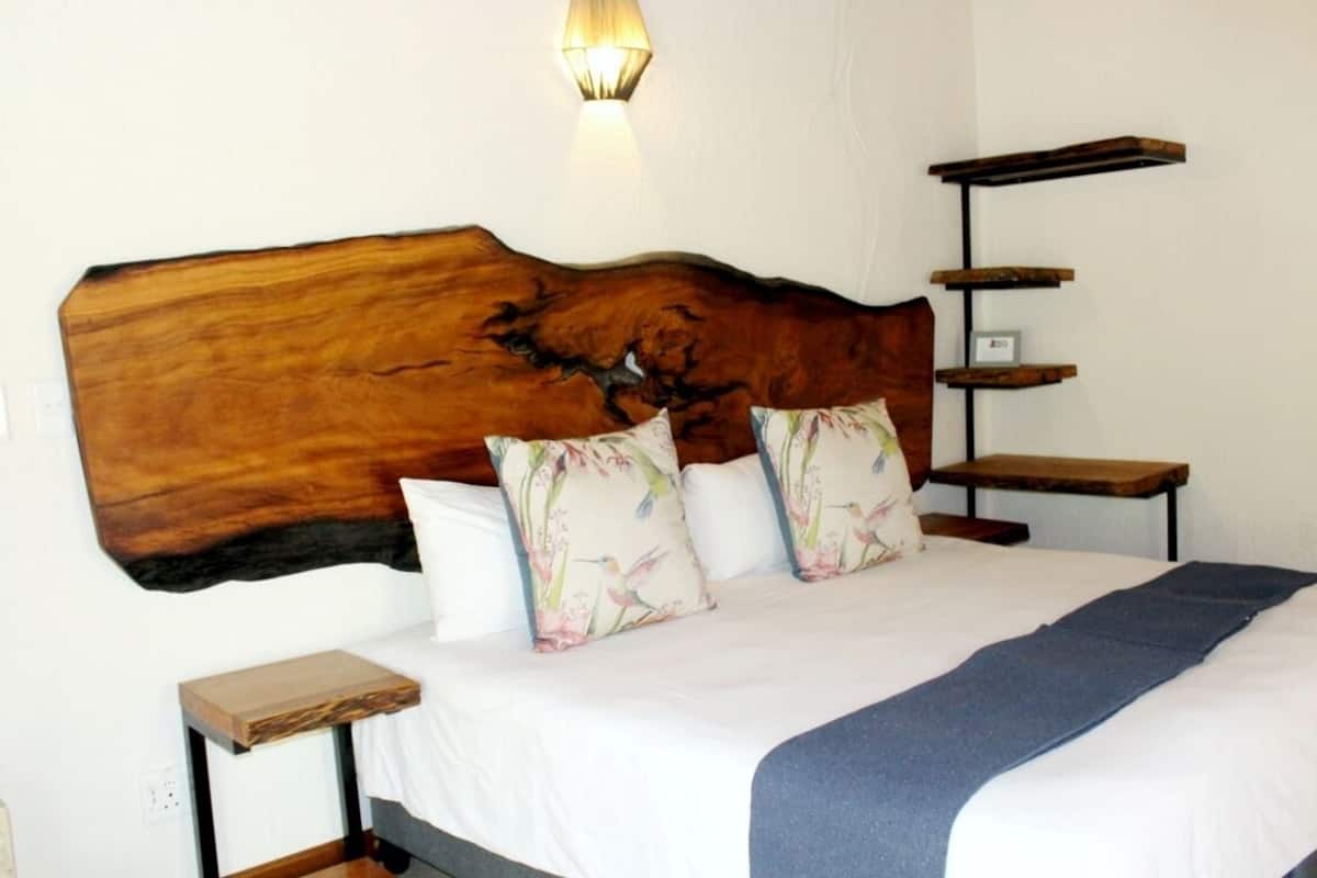 A bedroom with a large wooden headboard, a bed with floral pillows, a bedside table, and a wall-mounted shelf.