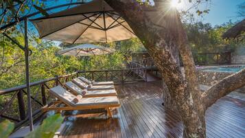 A wooden deck with lounge chairs and umbrellas, overlooking a pool area.