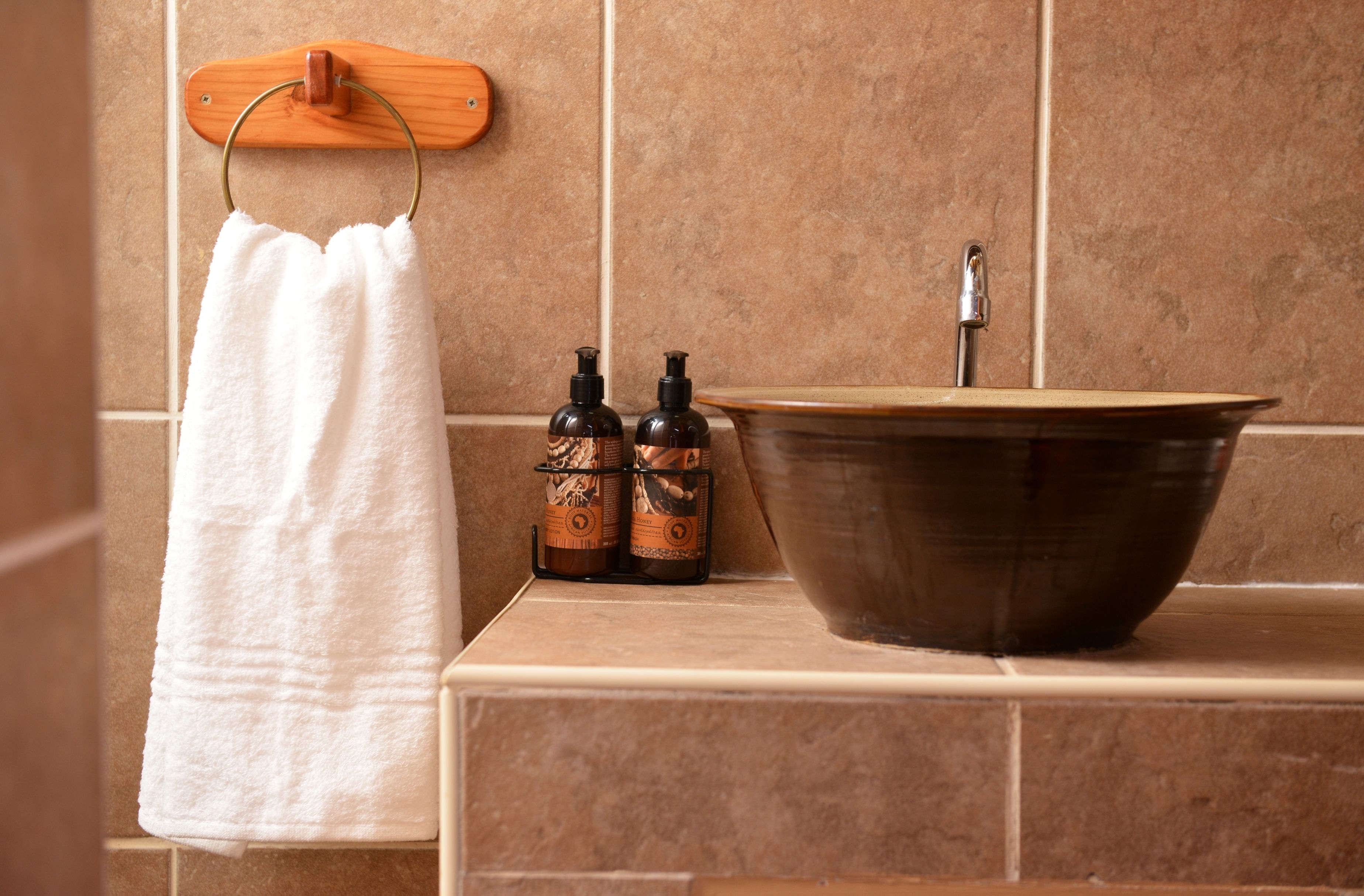 A bathroom with a wooden towel rack, a white towel, two soap dispensers, and a large ceramic sink.