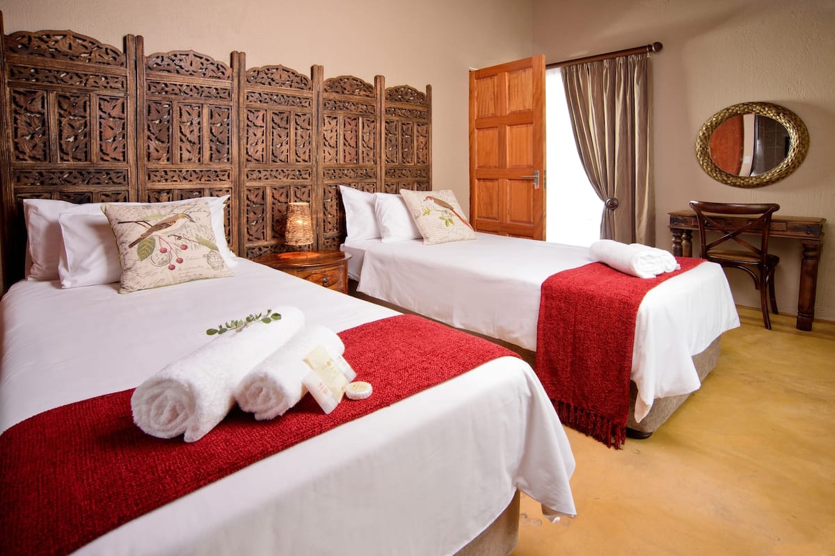 A hotel room with two beds, each with white linens and red blankets, a wooden headboard, a wooden desk with a mirror, and a wooden floor.