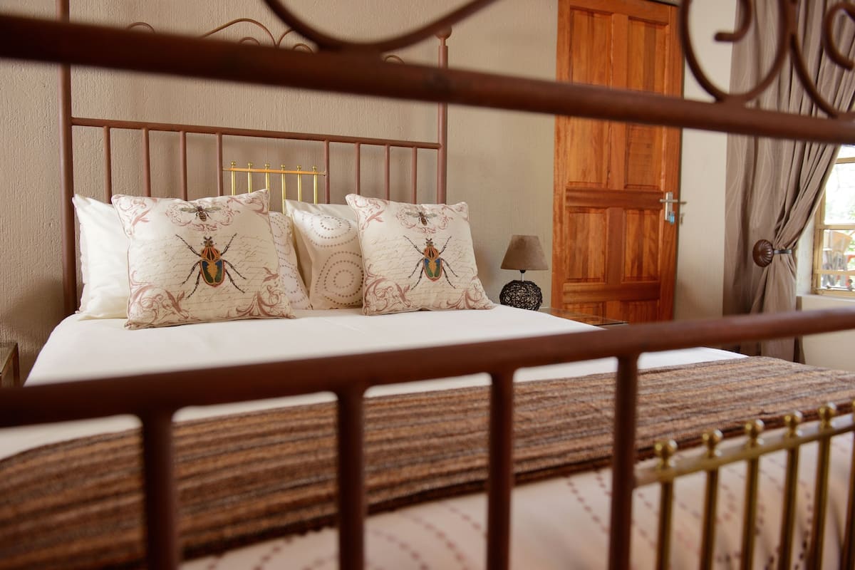 A bed with four pillows featuring a dragonfly design, a wooden headboard, and a nightstand with a lamp.