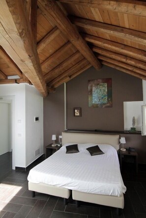 Une chambre à coucher avec un grand lit, des poutres apparentes en bois au plafond, un tableau au mur et une table de chevet avec une lampe.