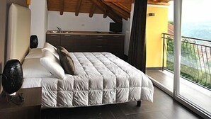 A bedroom with a large bed, a wooden ceiling, a balcony with a view, and a kitchen area.