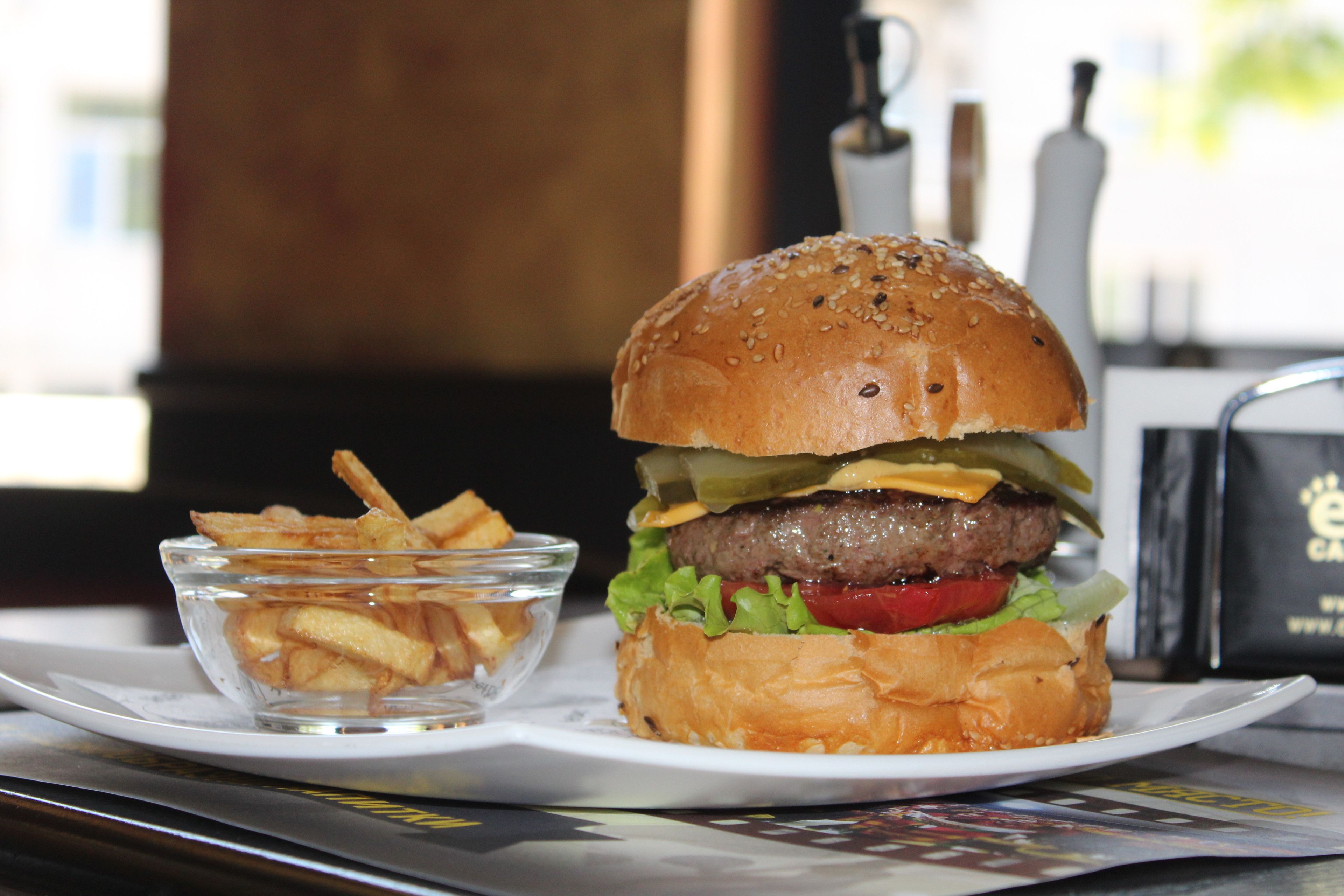 Hamburguesa con lechuga, tomate y queso, acompañada de un tazón pequeño de papas fritas sobre un plato blanco.
