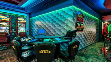 Un espace de jeux de casino comprenant plusieurs machines à sous, une table centrale entourée de chaises et un mur à la texture particulière.