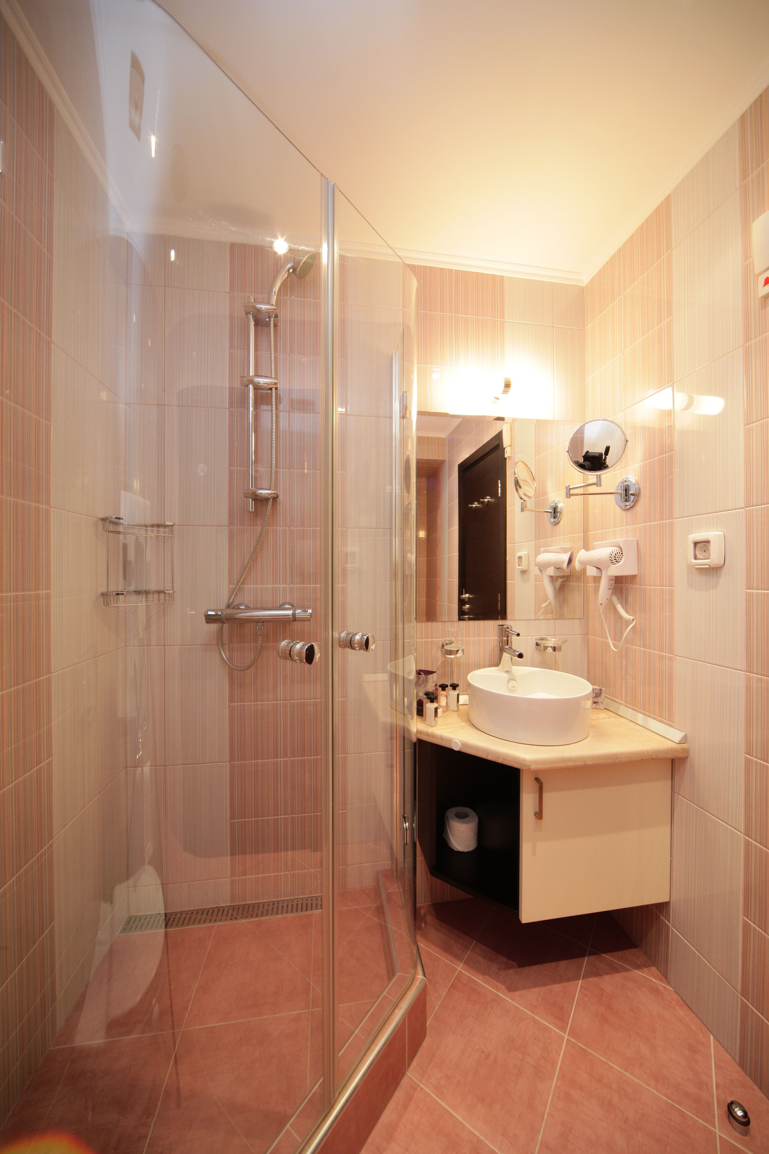 A modern bathroom with a glass-enclosed shower, a sink with a vanity, and a mirror with a hairdryer mounted on the wall.