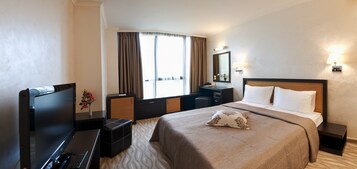 Habitación de hotel con una cama grande, un escritorio con computadora, cómoda y una ventana con cortinas.