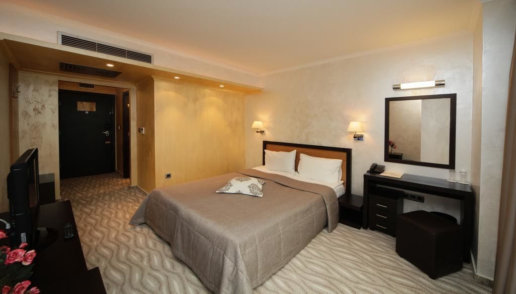 A hotel room with a bed, bedside table, mirror, and a desk with a chair.