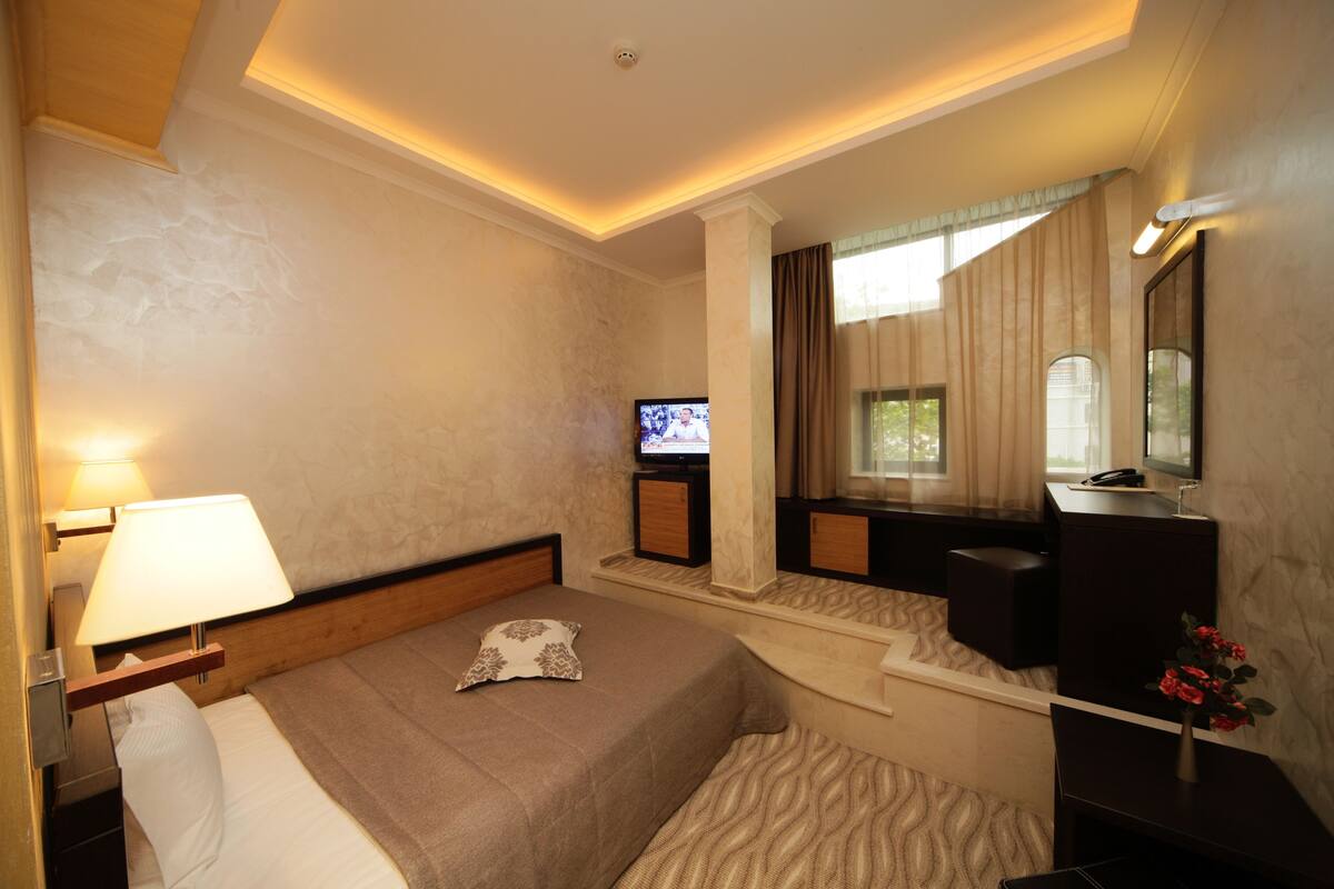 A hotel room with a bed, a TV, a desk, and a mirror.
