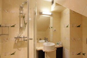 Un bagno con doccia a vetro, lavandino con specchio sopra e piastrelle decorative con motivi floreali.
