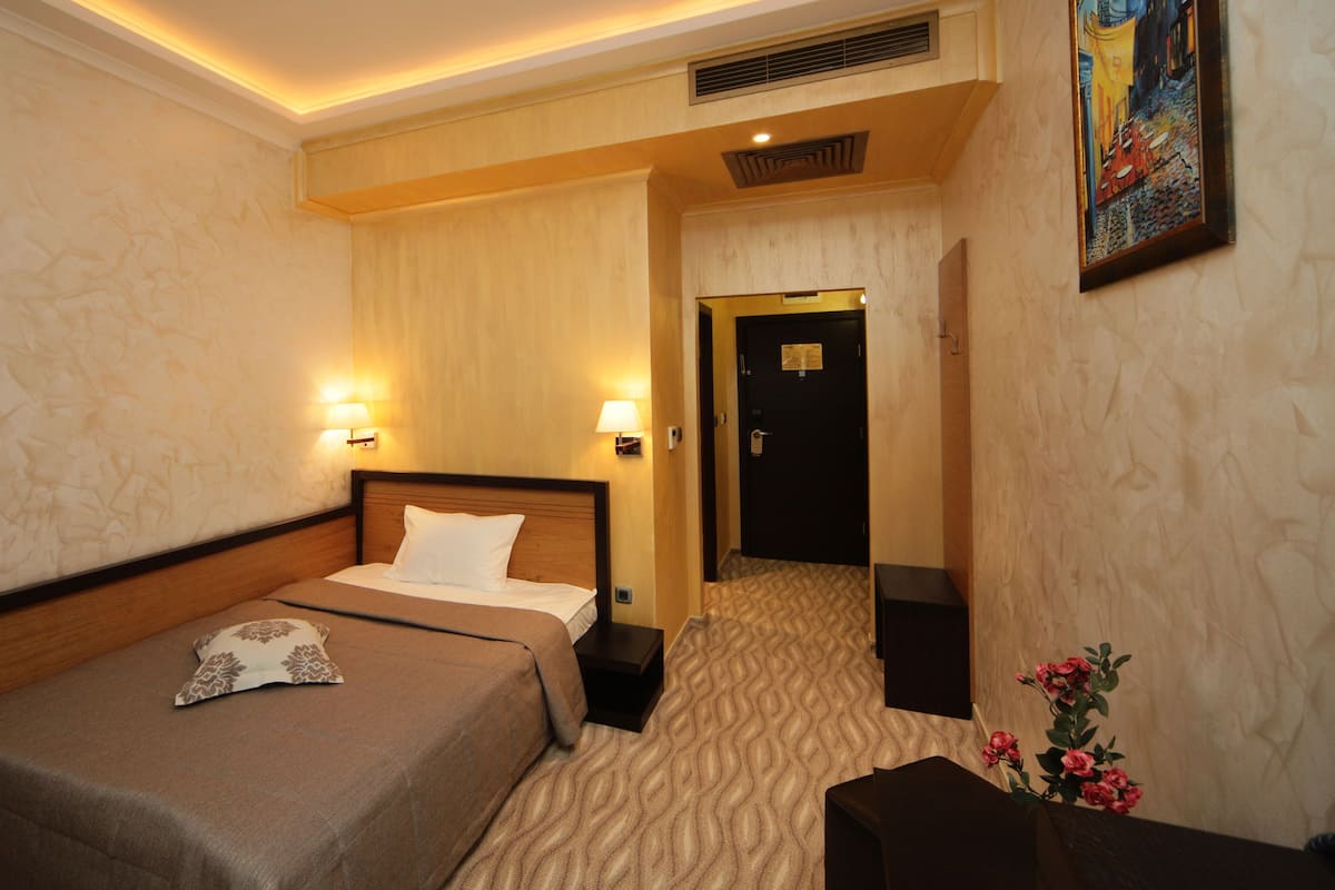 A hotel room with a bed, bedside lamps, a door, and a painting on the wall.
