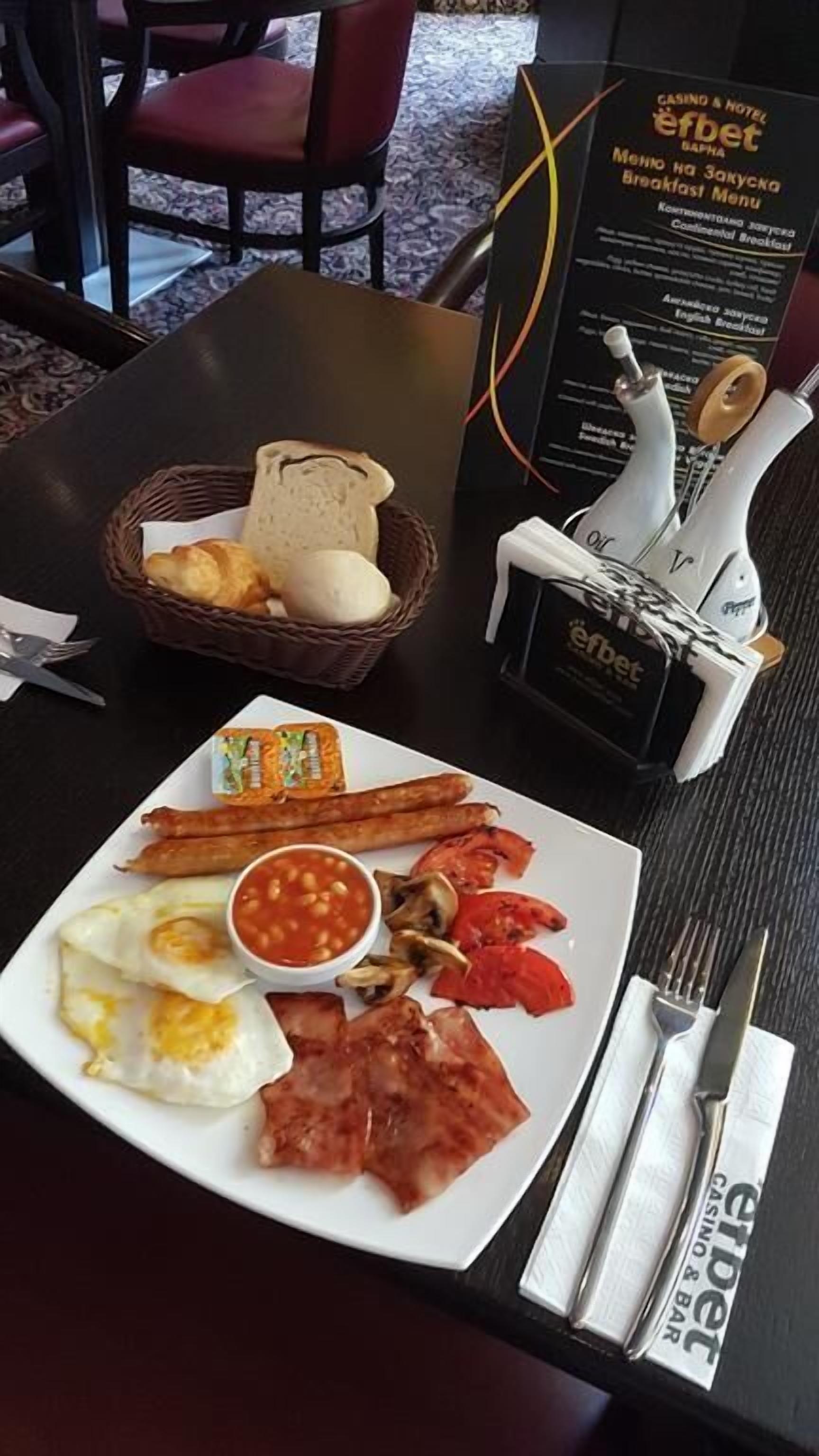 A breakfast plate with eggs, sausages, tomatoes, and beans, a basket of bread, and a menu stand with a pen holder.