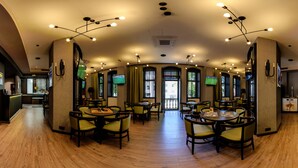 A spacious dining area with multiple tables and chairs, a central chandelier, and large windows with curtains. - EfBet Hotel (Varna)