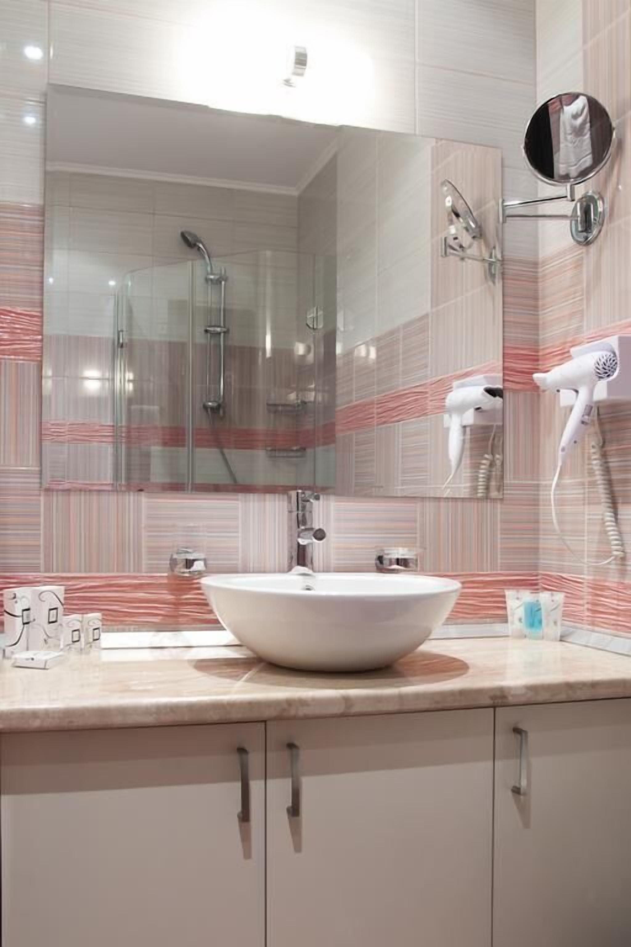 Un baño moderno con un espejo grande, una ducha con cerramiento de vidrio y un lavabo blanco.