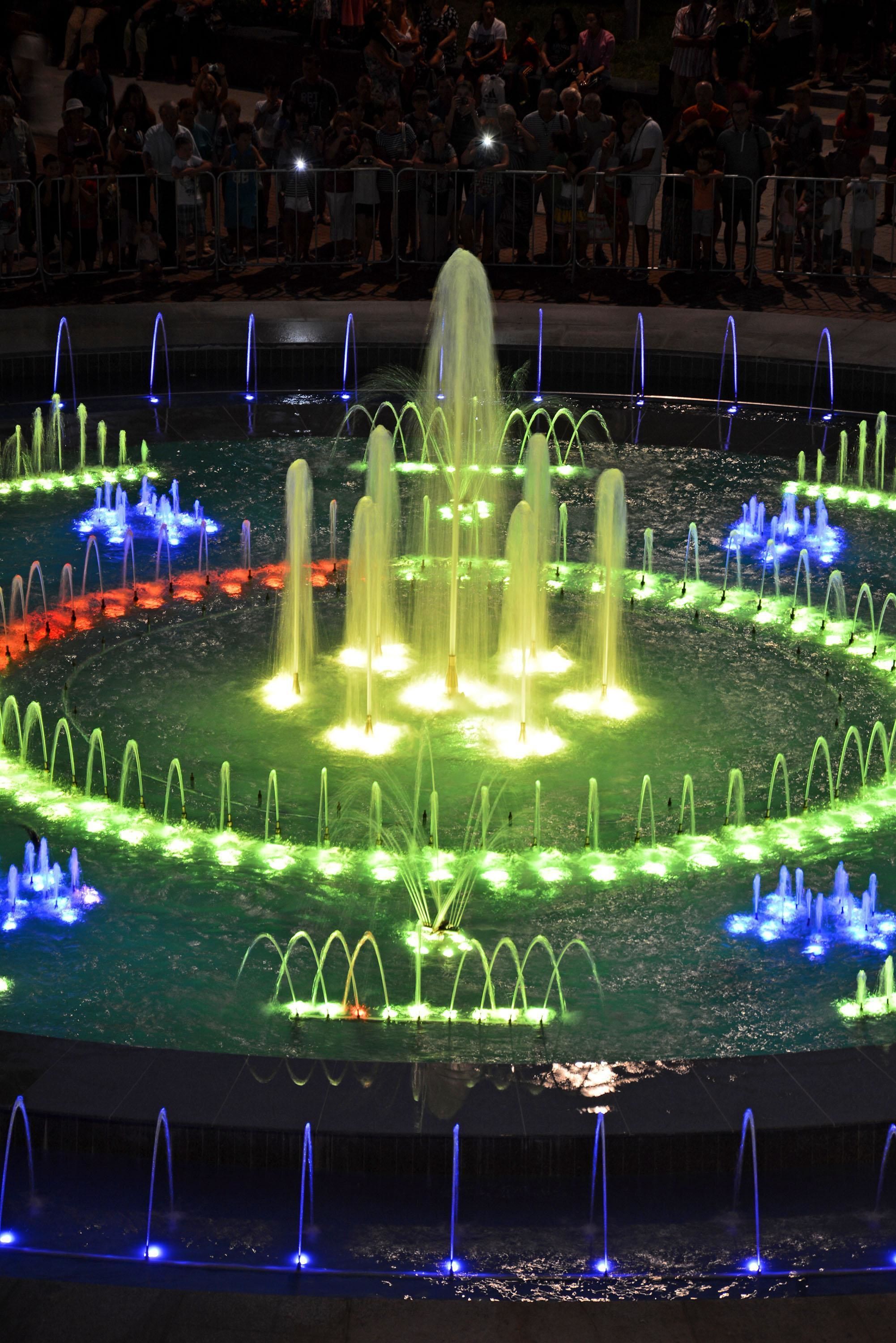 A nighttime fountain display with multiple water jets illuminated in various colors.