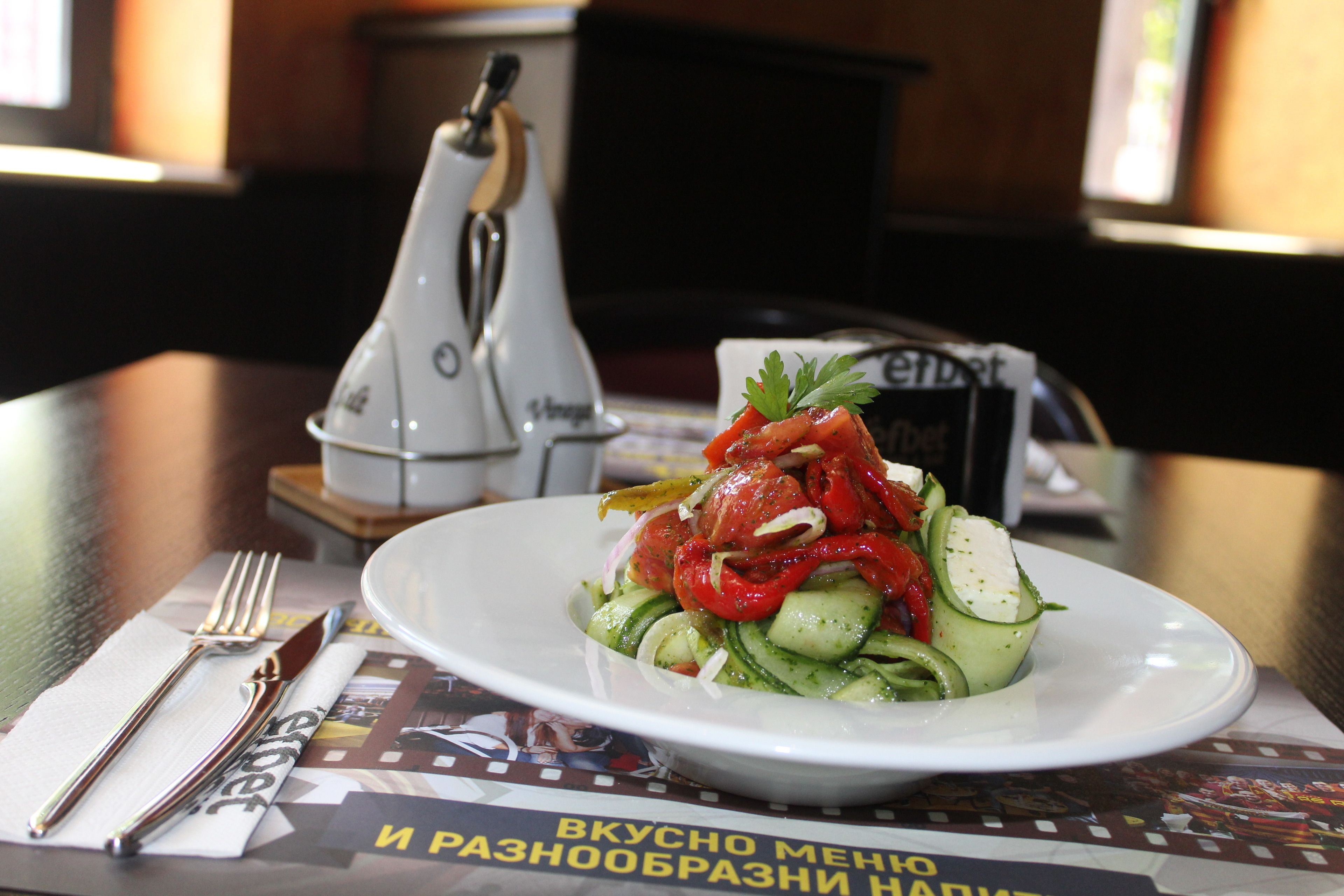 Un plato de ensalada sobre una mesa, junto con un menú y salero y pimentero.