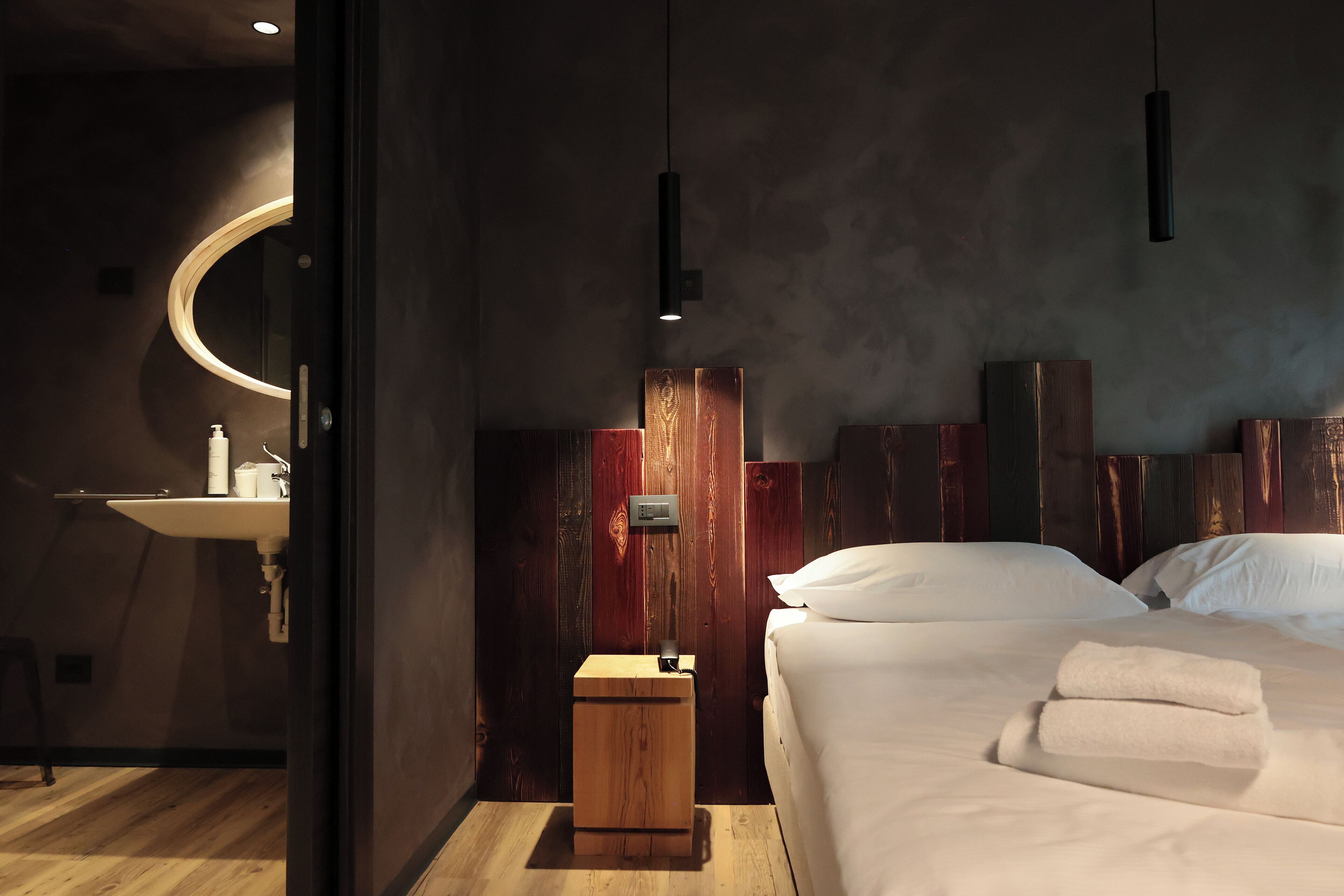 A modern bedroom with a wooden headboard, a bedside table, and a bed with white linens.