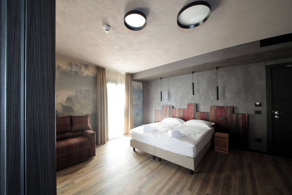 A modern bedroom with a large bed, a sofa, and a wooden floor.