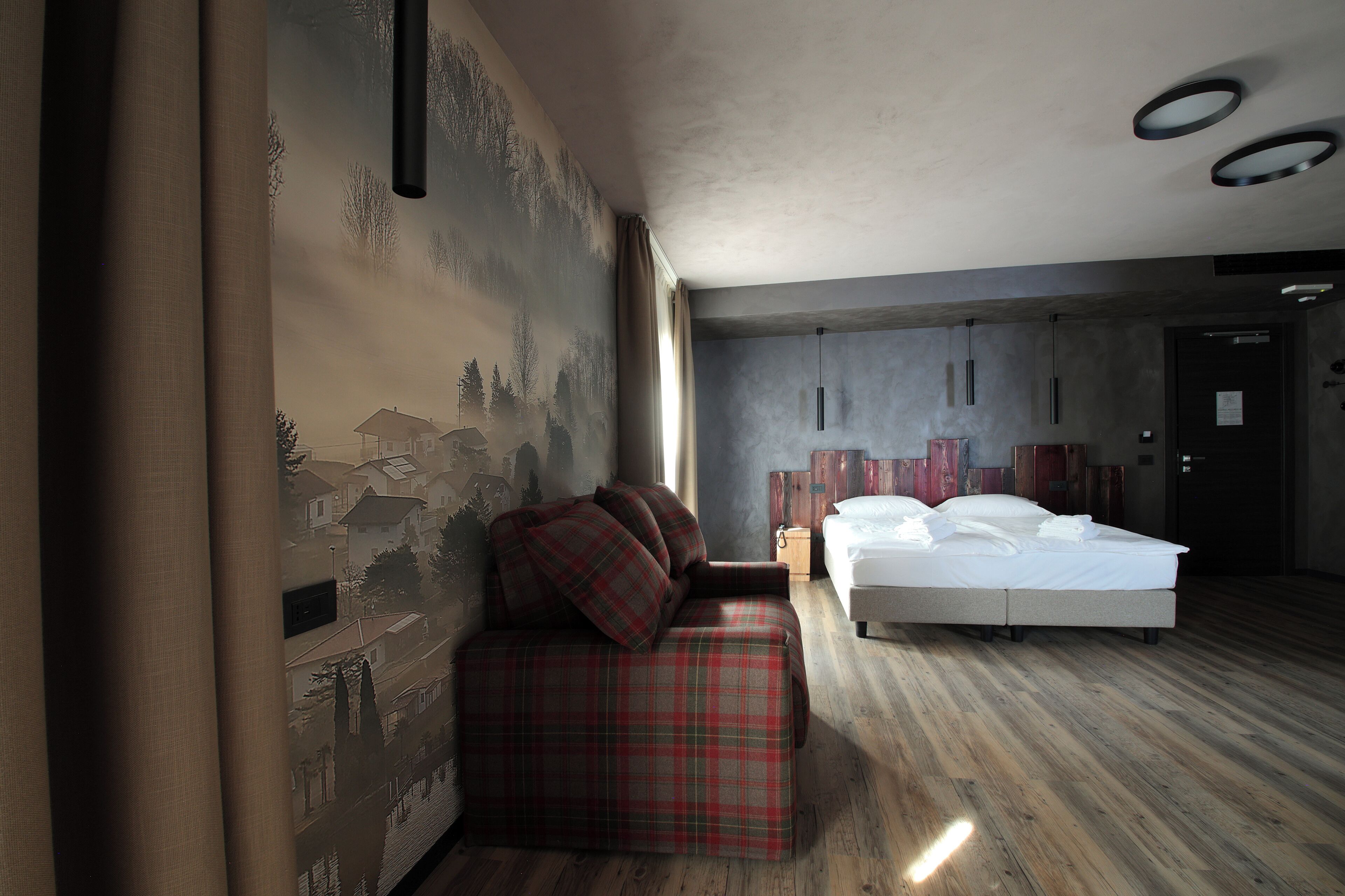 Una habitación de hotel moderna con piso de madera, una cama con ropa blanca, un sofá de cuadros rojos y un mural en la pared.