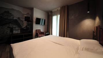 A hotel room with a large bed, a chair, a TV mounted on the wall, and a painting of a mountain scene.