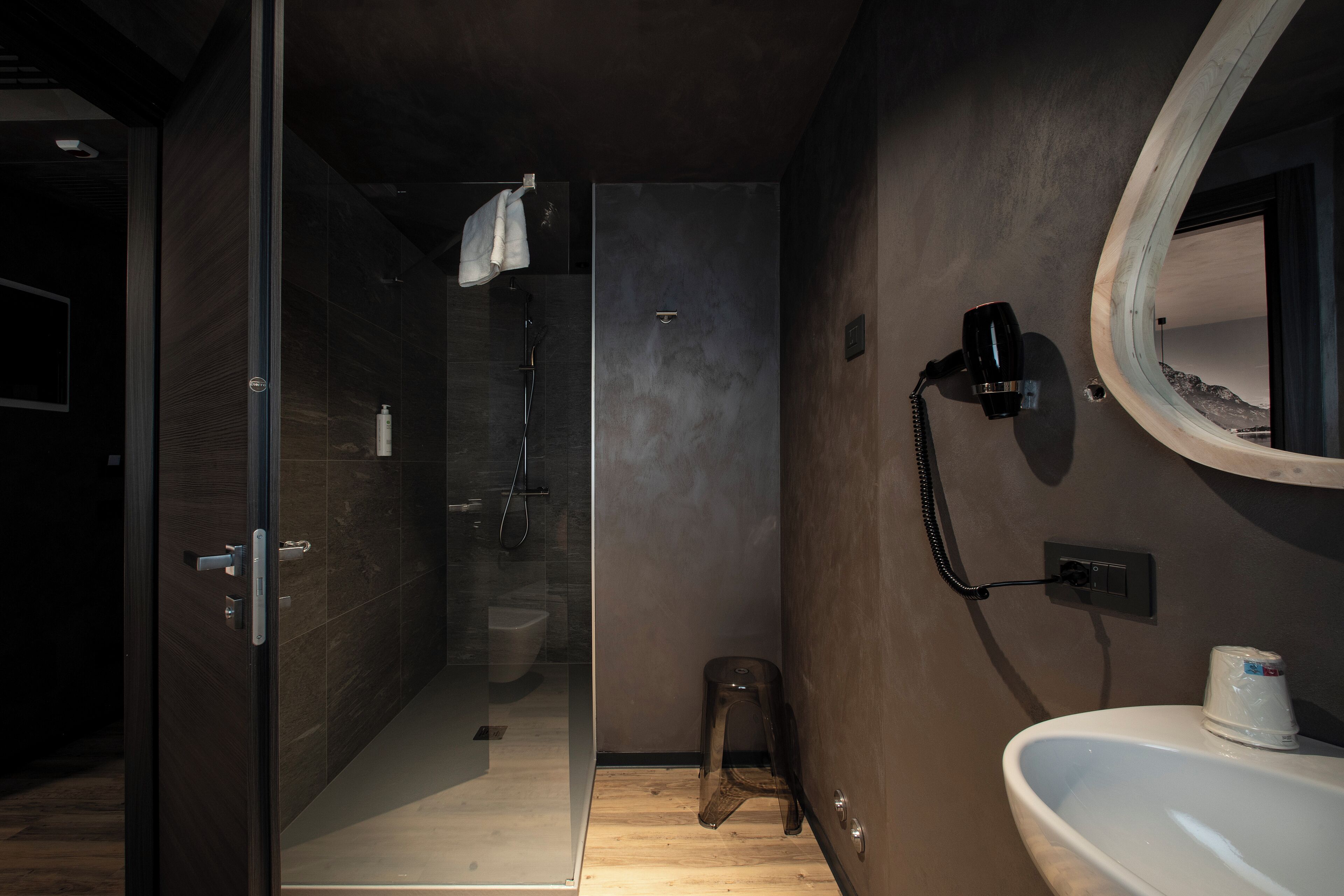 Un baño moderno con cabina de ducha de vidrio, un lavamanos blanco y un secador de pelo en una estación de carga mural.