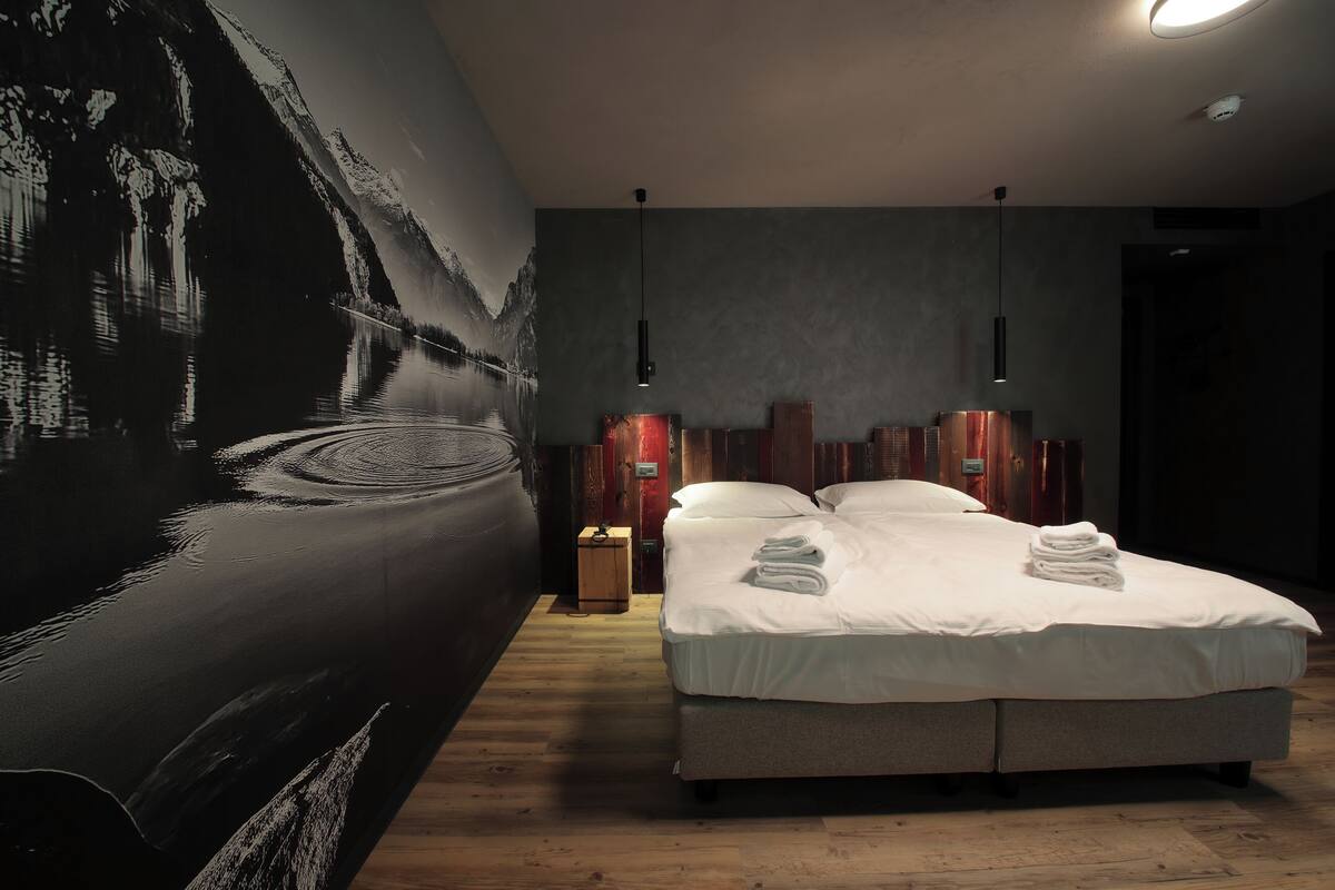 A modern bedroom with a large bed, a wooden floor, and a cityscape mural on the wall.