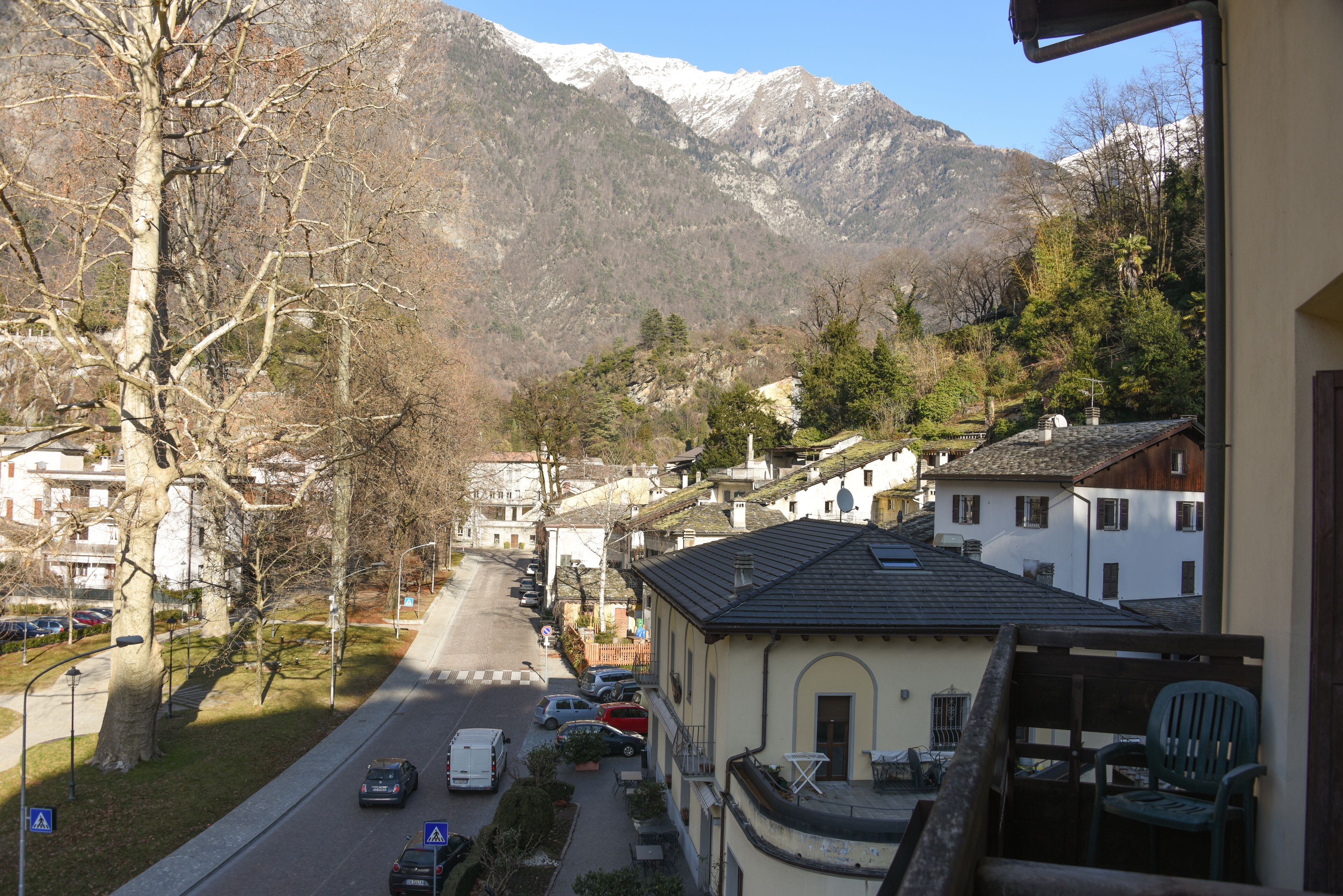 Una strada residenziale con case, cielo sereno e montagne sullo sfondo.