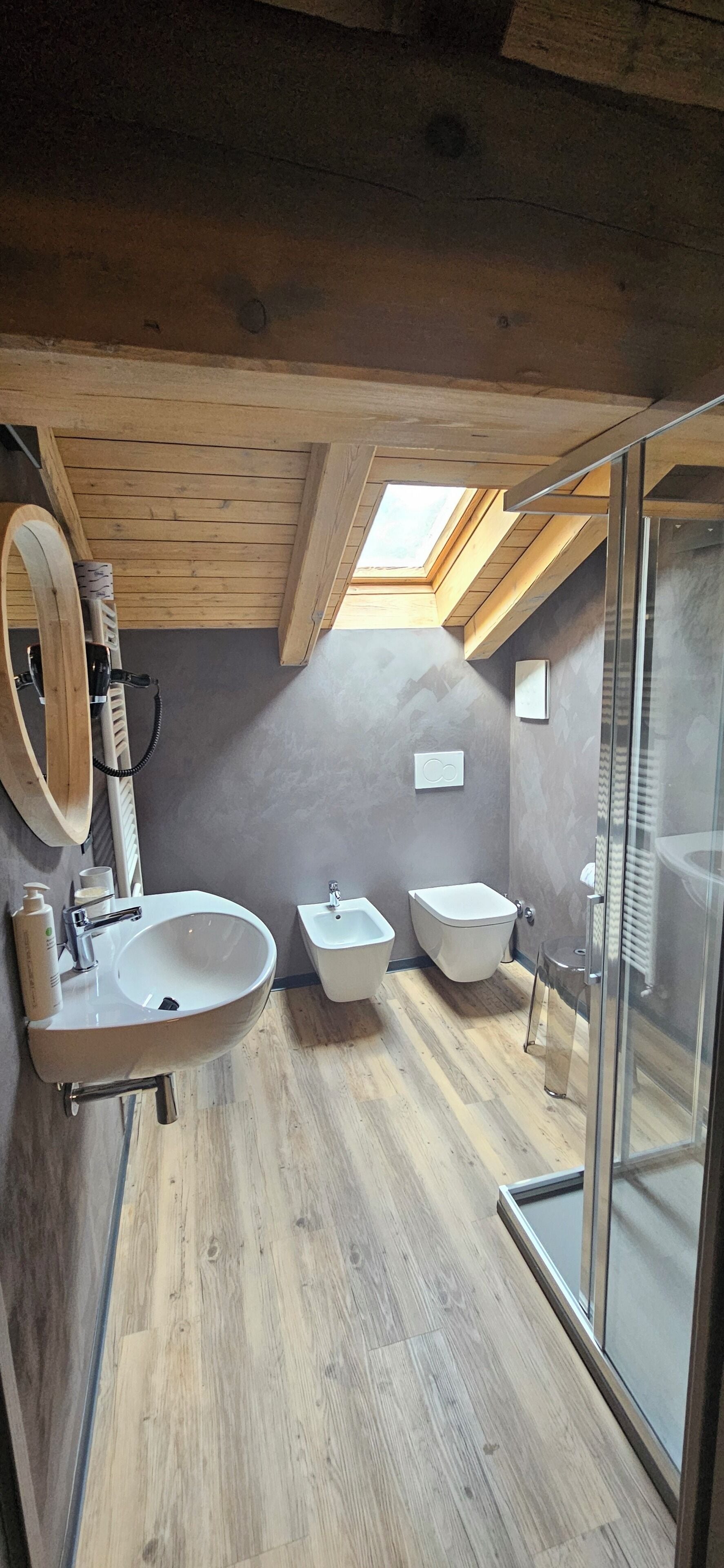 Un baño moderno con tragaluz, techo de madera y cabina de ducha de vidrio.